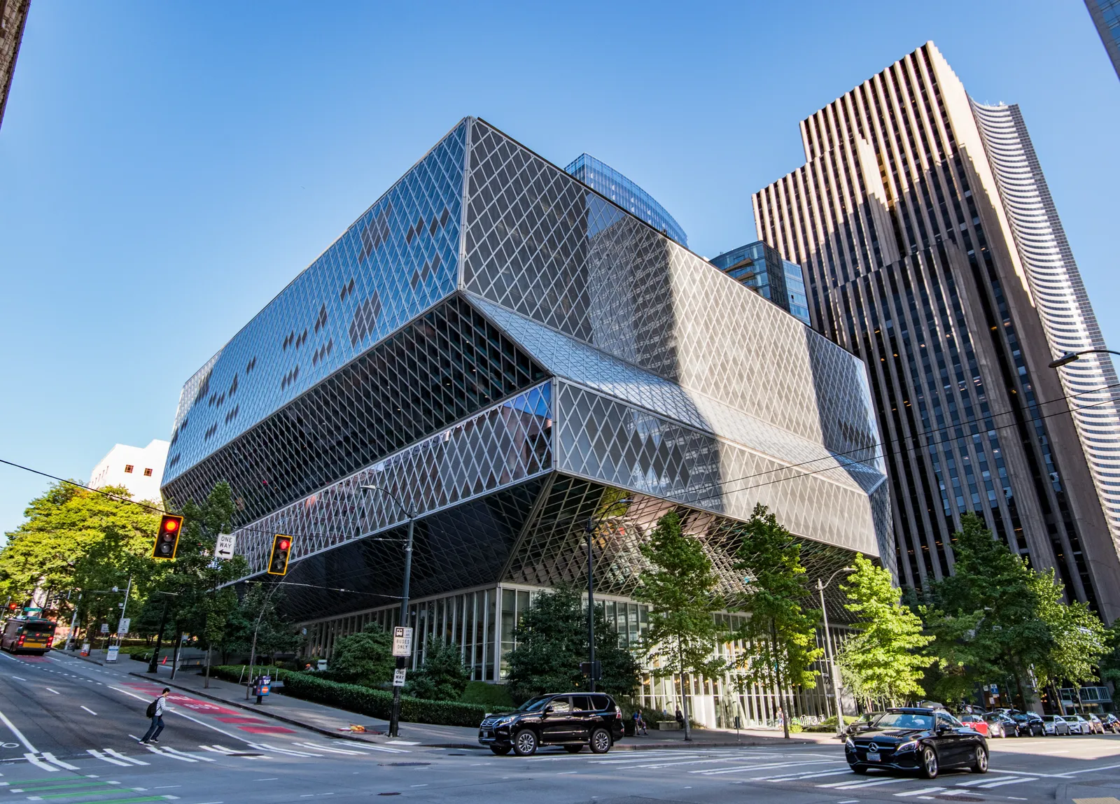 The Seattle Central Library's angled glass-and-steel diamond grid seen from the corner of Fourth Avenue, its upper floors cantilevered out over the street