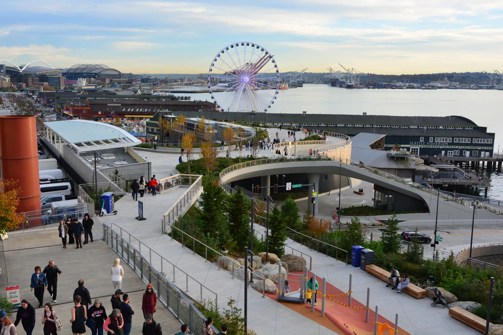 The Overlook Walk in Seattle, a wide concrete deck curving down over Alaskan Way toward the Elliott Bay piers, with the Great Wheel and the bay beyond it
