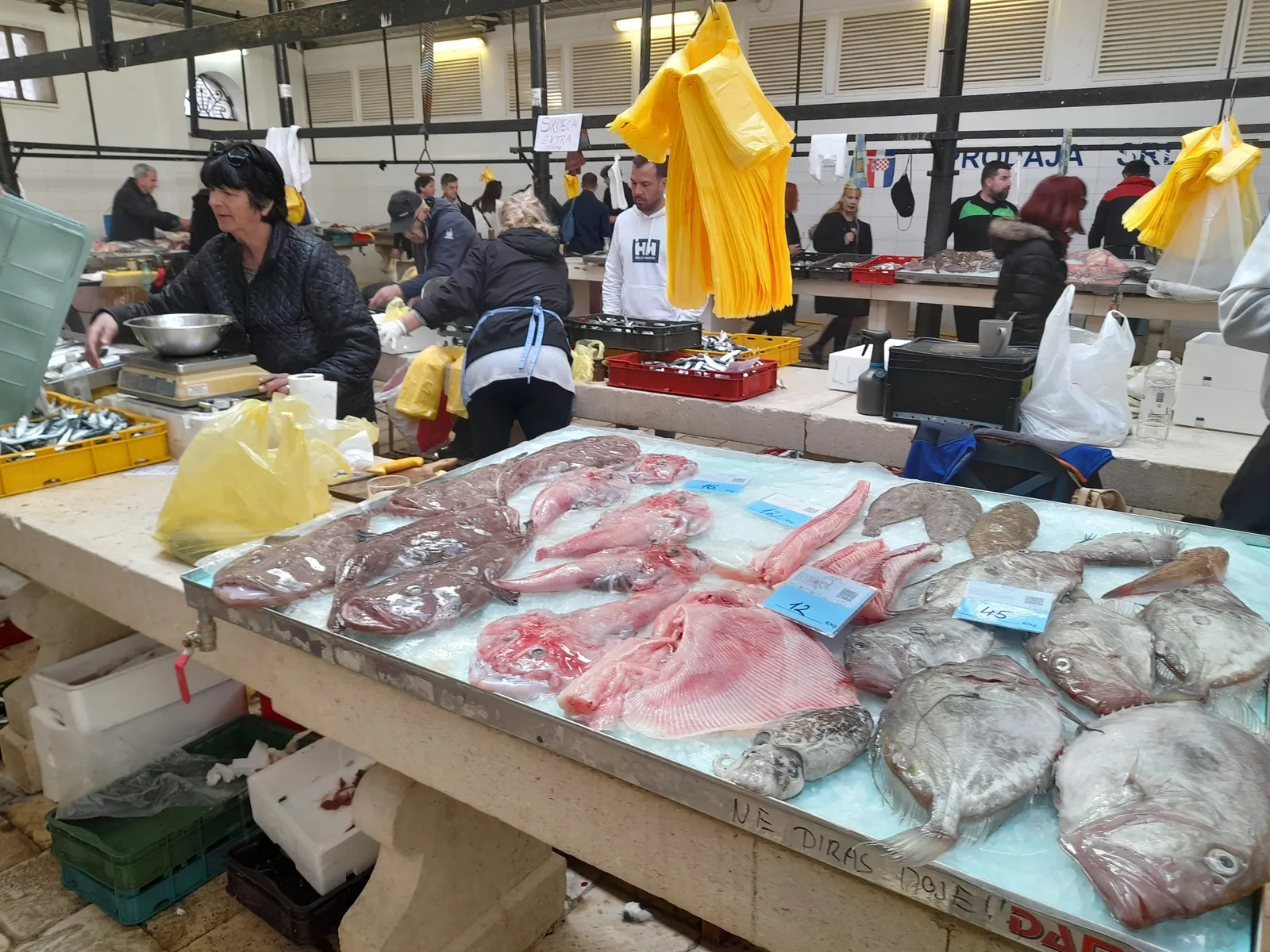 Split's covered fish market, a long marble counter laid with whole fish and fillets on ice, traders in yellow oilskins working behind it under the hall's open roof