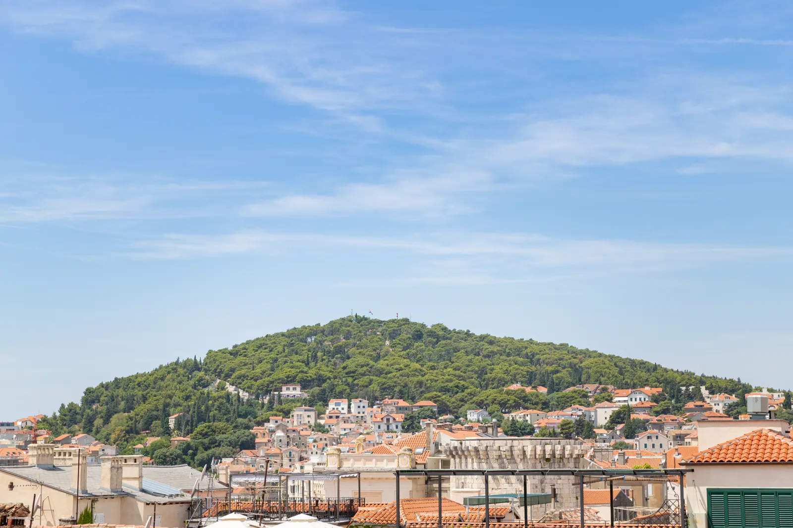 The wooded hill of Marjan rising green and round above the rooftops of Split, houses climbing partway up its lower slopes under a blue sky