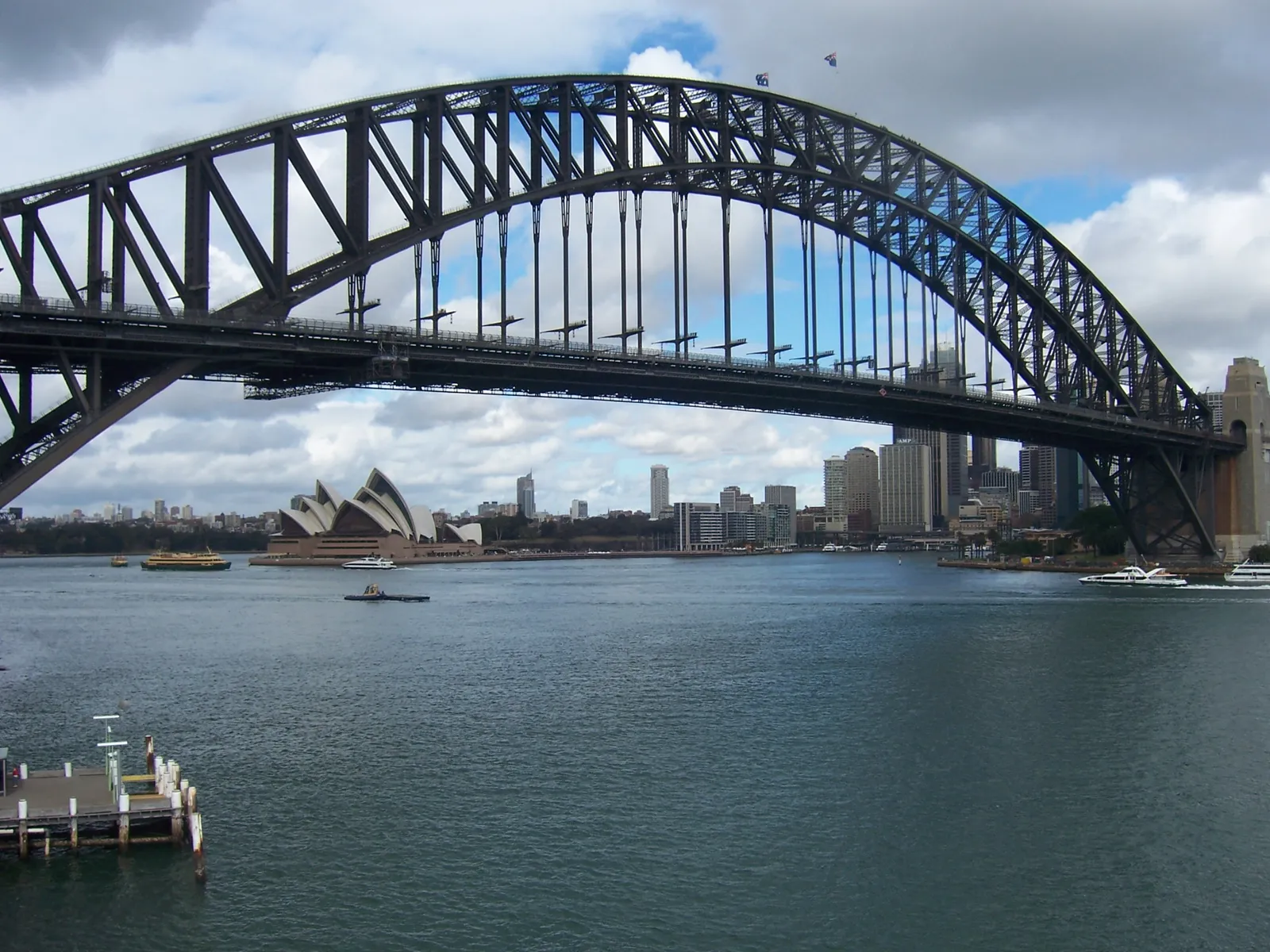 The steel arch of the Sydney Harbour Bridge seen from Milsons Point, with the Opera House and the city skyline across the harbour beneath it