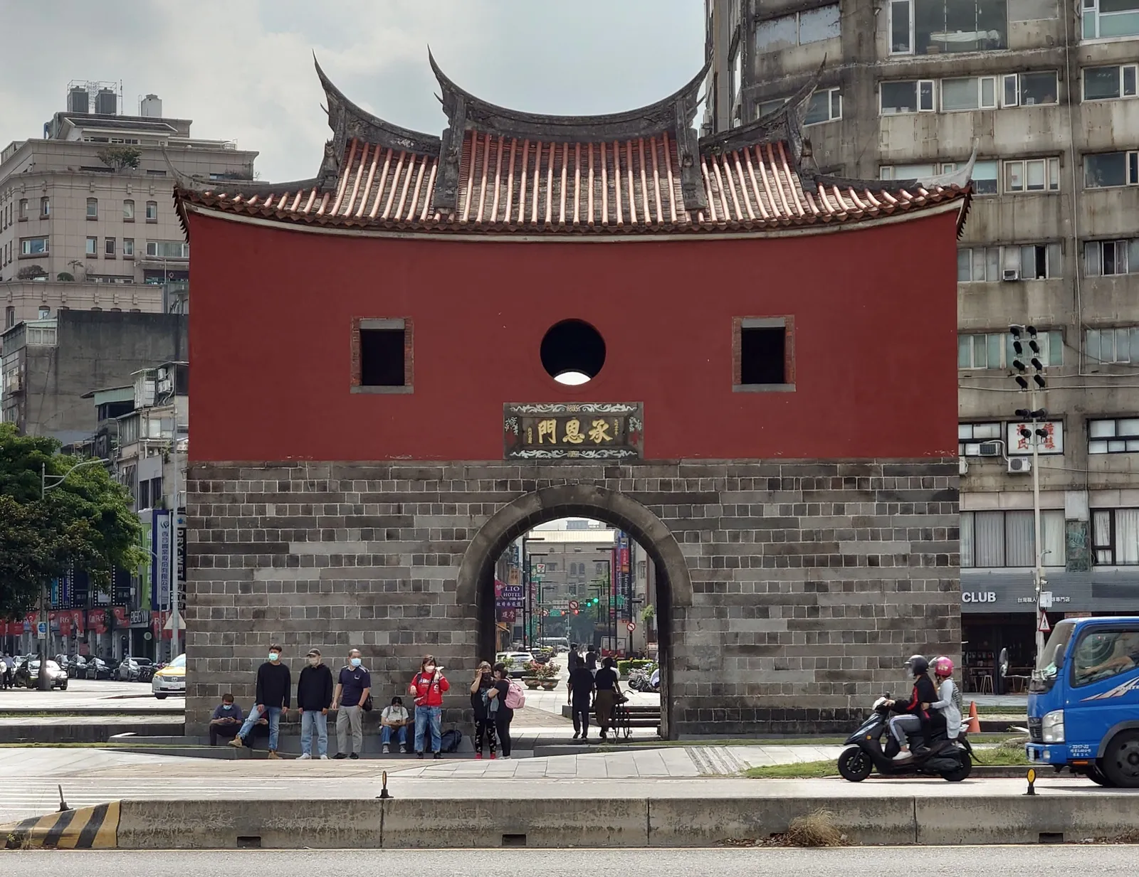 Beimen, Taipei's North Gate, a squat red-walled gatehouse on a stone base with a swept tiled roof, standing on a traffic island with modern buildings around it
