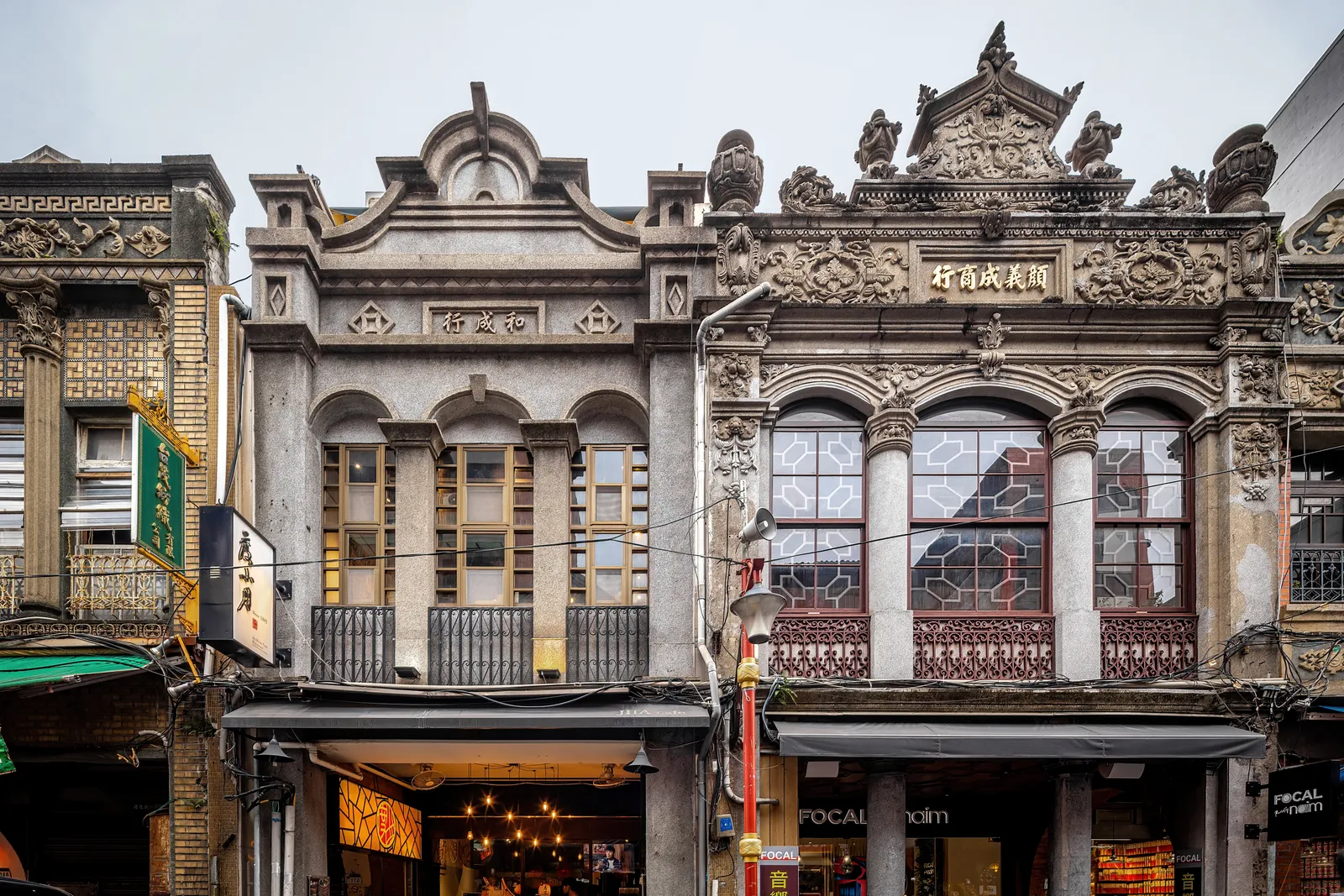 Two ornate shophouse facades on Dihua Street in Taipei, with carved gables, pilasters and tiled panels above ground-floor shops set back under an arcade