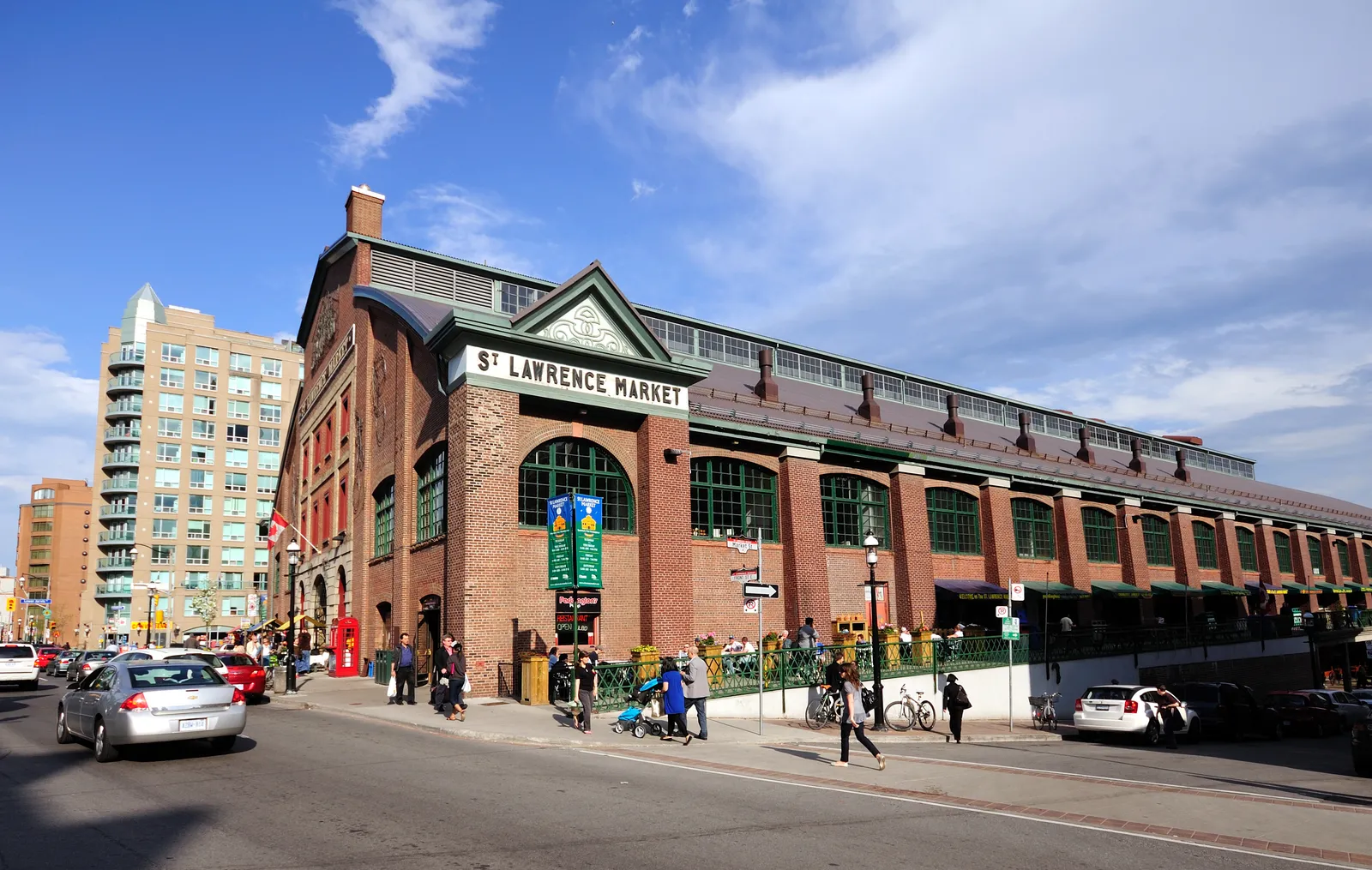 The long red-brick south hall of St. Lawrence Market in Toronto with its name in white letters along the roofline, green window frames and shoppers on the pavement outside