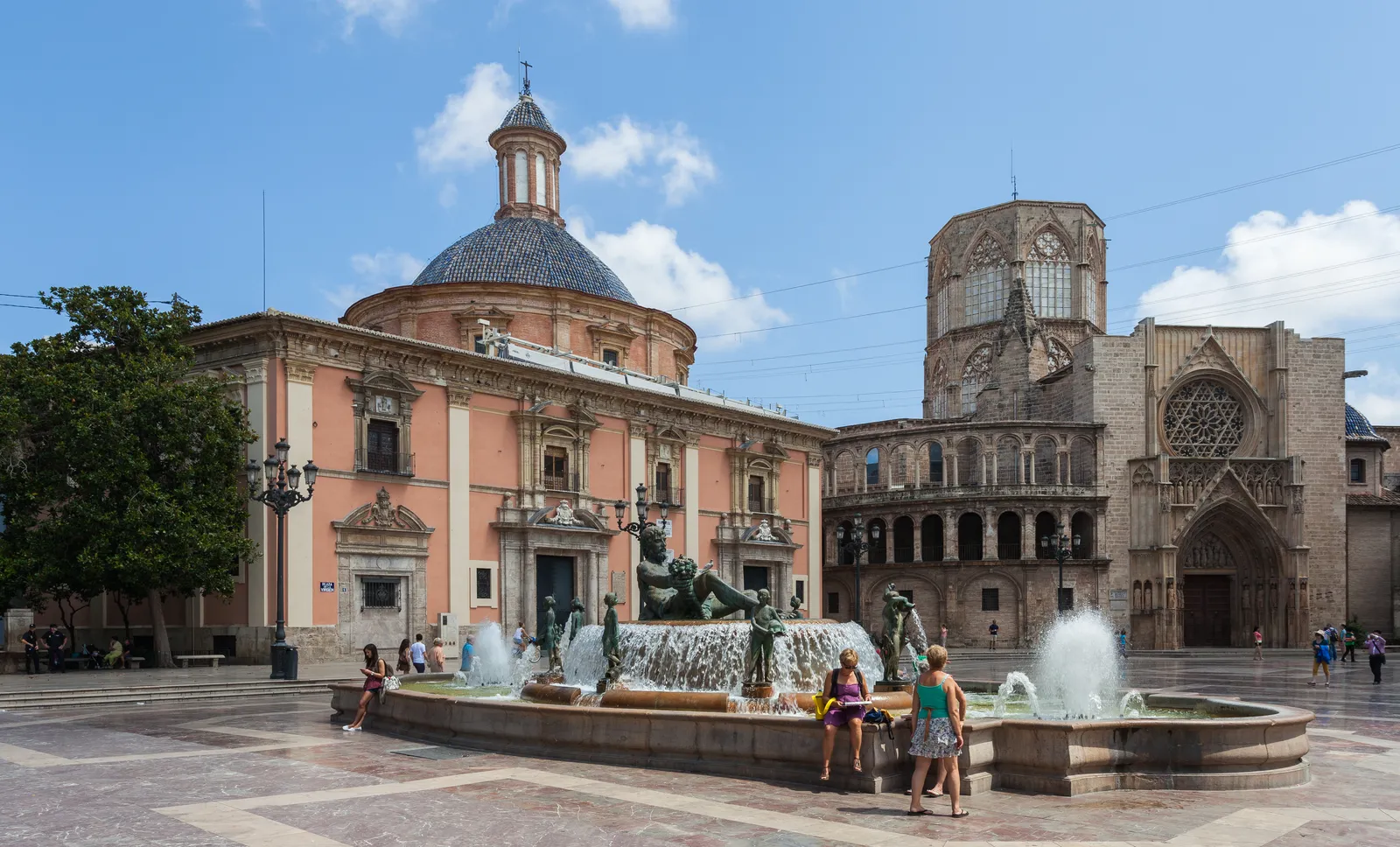 The Plaza de la Virgen in Valencia, the domed pink basilica on the left, the cathedral's Gothic Apostles' Door and rose window on the right, and the Turia fountain running in the middle