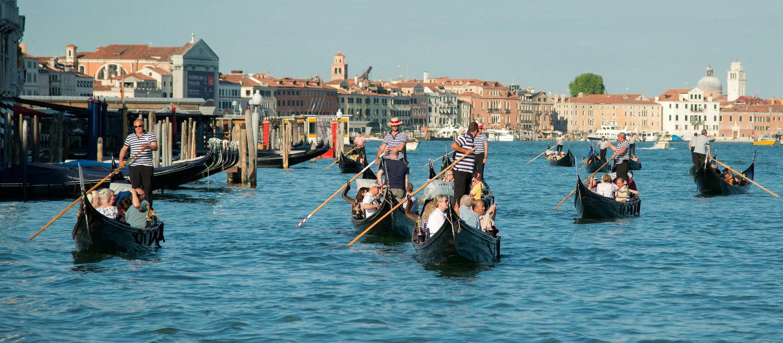 Several gondolas with rowers crossing the Grand Canal in Venice with the city skyline behind them