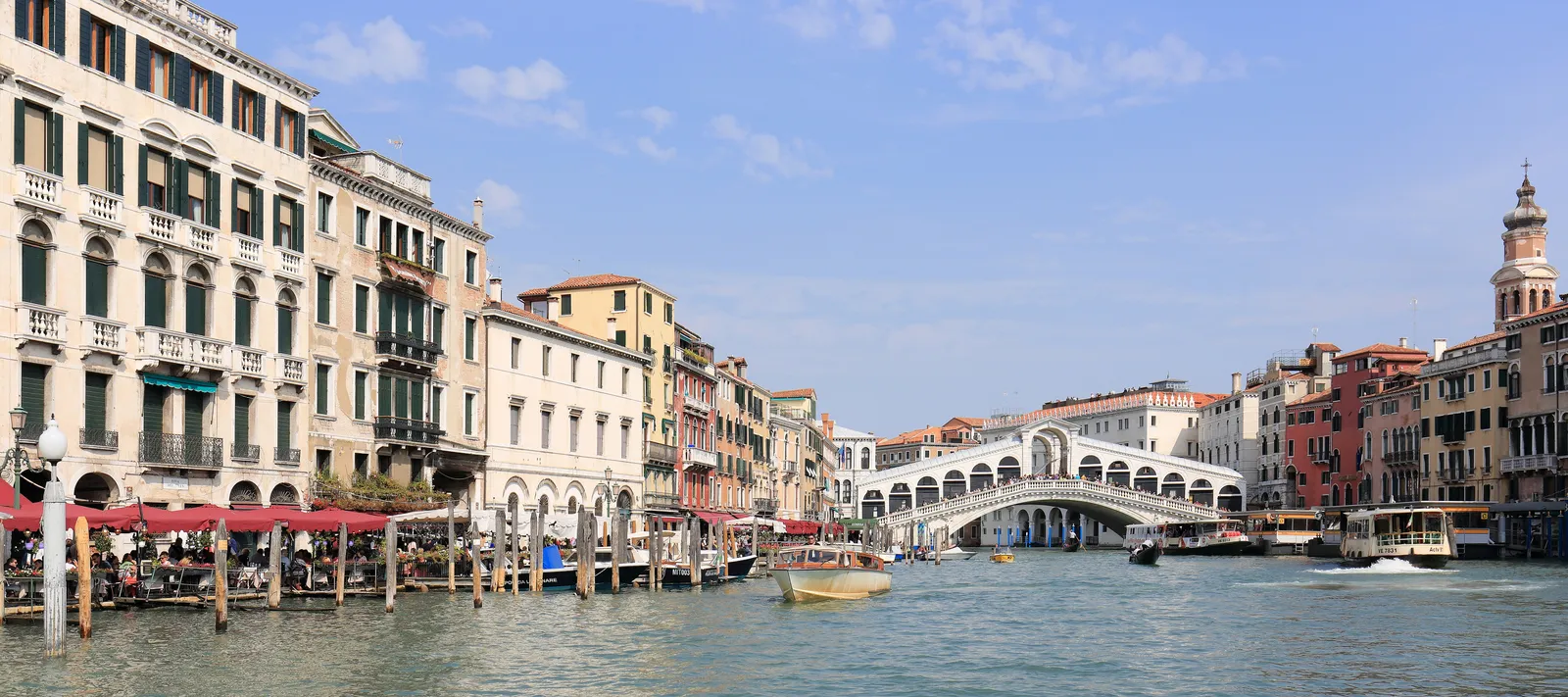 Wide view of the Grand Canal in Venice with the Rialto Bridge, water taxis, and vaporetti along the waterfront