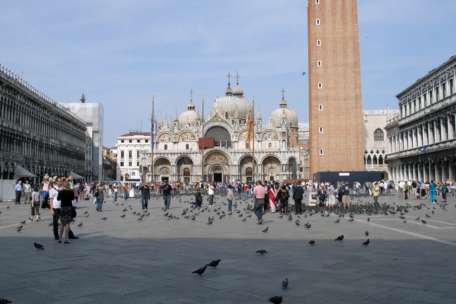 Piazza San Marco in Venice, the paved square filled with pigeons and visitors, with the five domes and marble front of St Mark's Basilica at the far end and the brick campanile rising beside it
