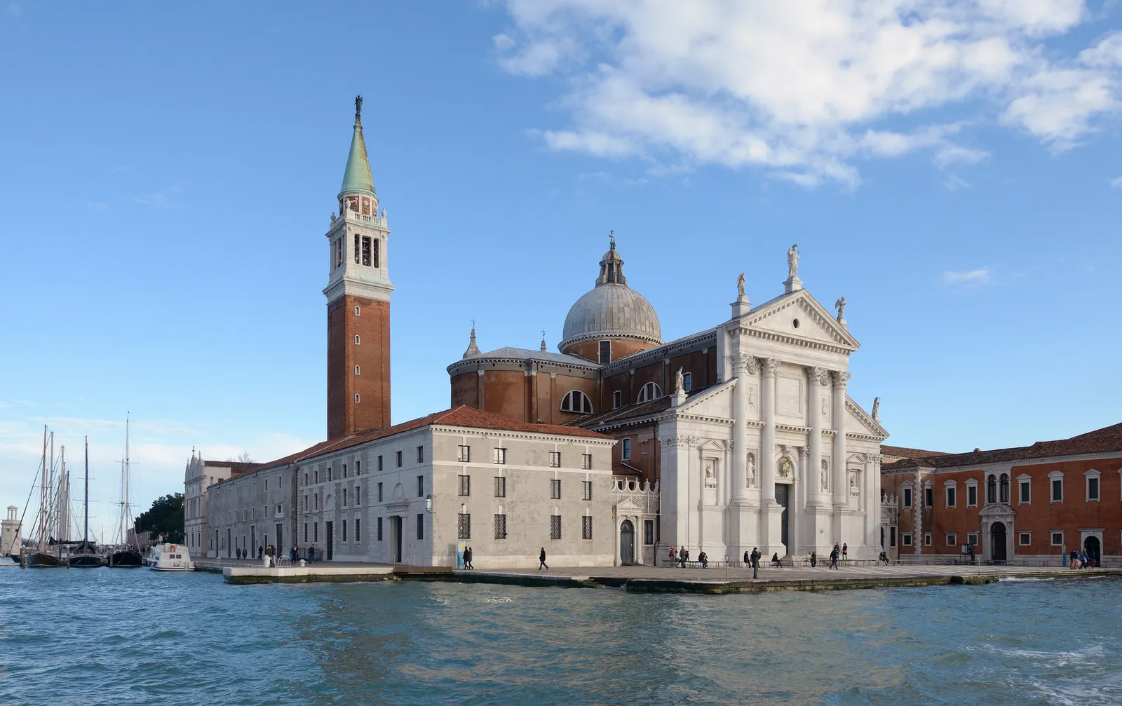 The island of San Giorgio Maggiore in Venice seen across the water, Palladio's white stone church front beside its brick bell tower with the green spire, and a low quay running along the front of the island