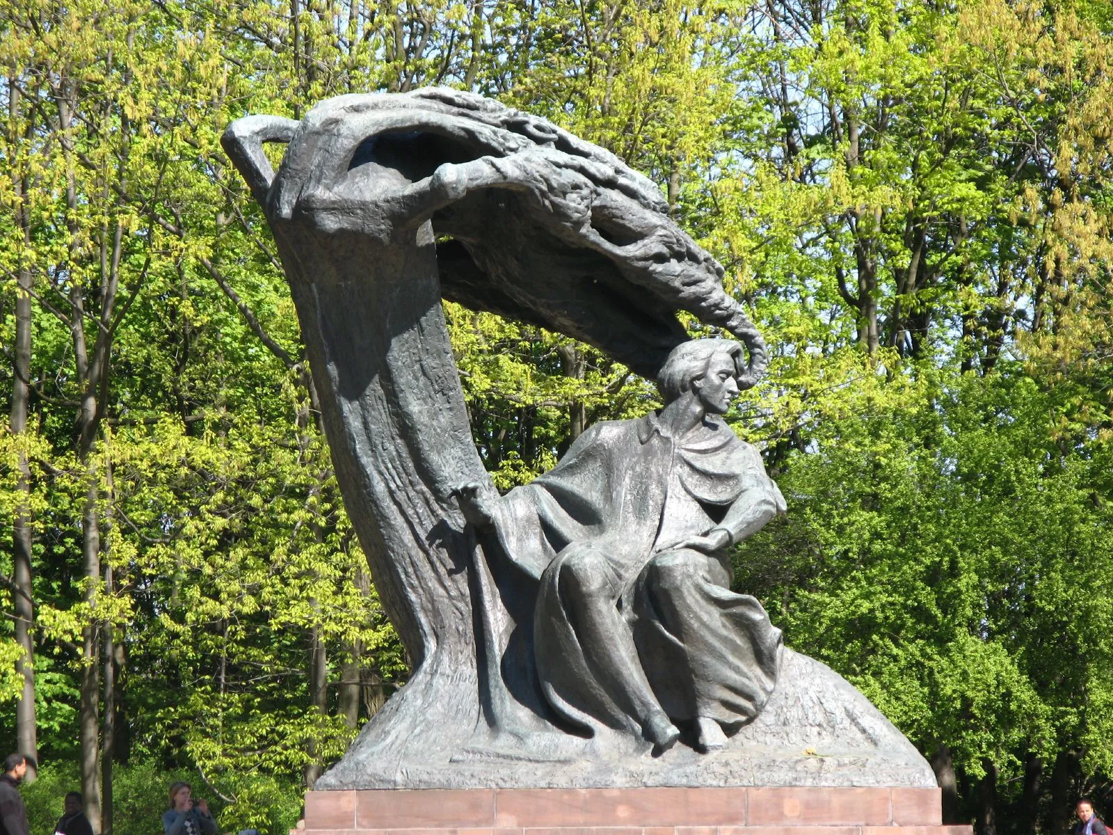 The bronze Chopin monument in Warsaw's Łazienki Park, the composer seated beneath a windswept willow that curves over him, surrounded by summer foliage