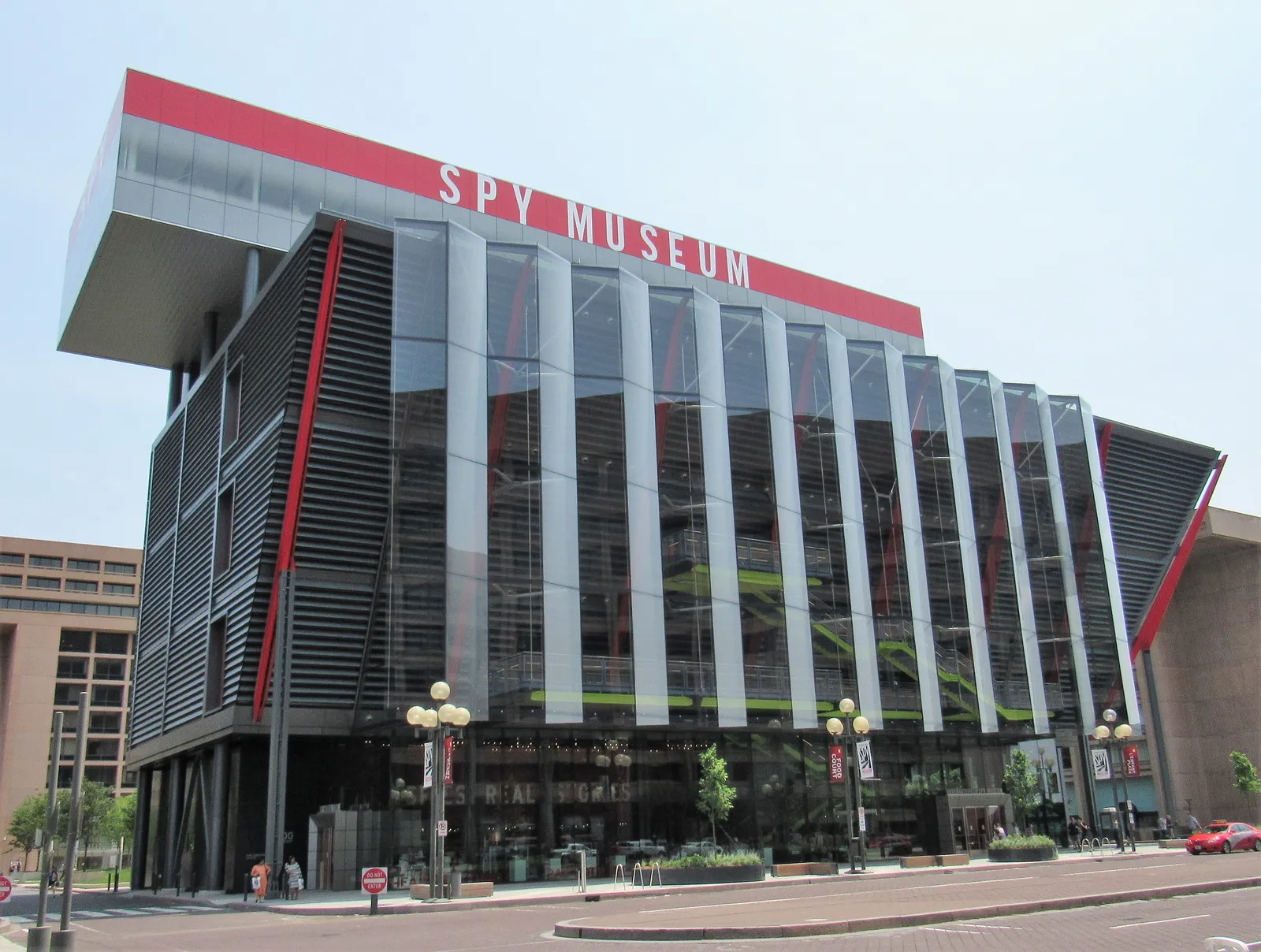The International Spy Museum in Washington, a glass box braced with red and black steel fins, with SPY MUSEUM lettered across a red band along the roofline