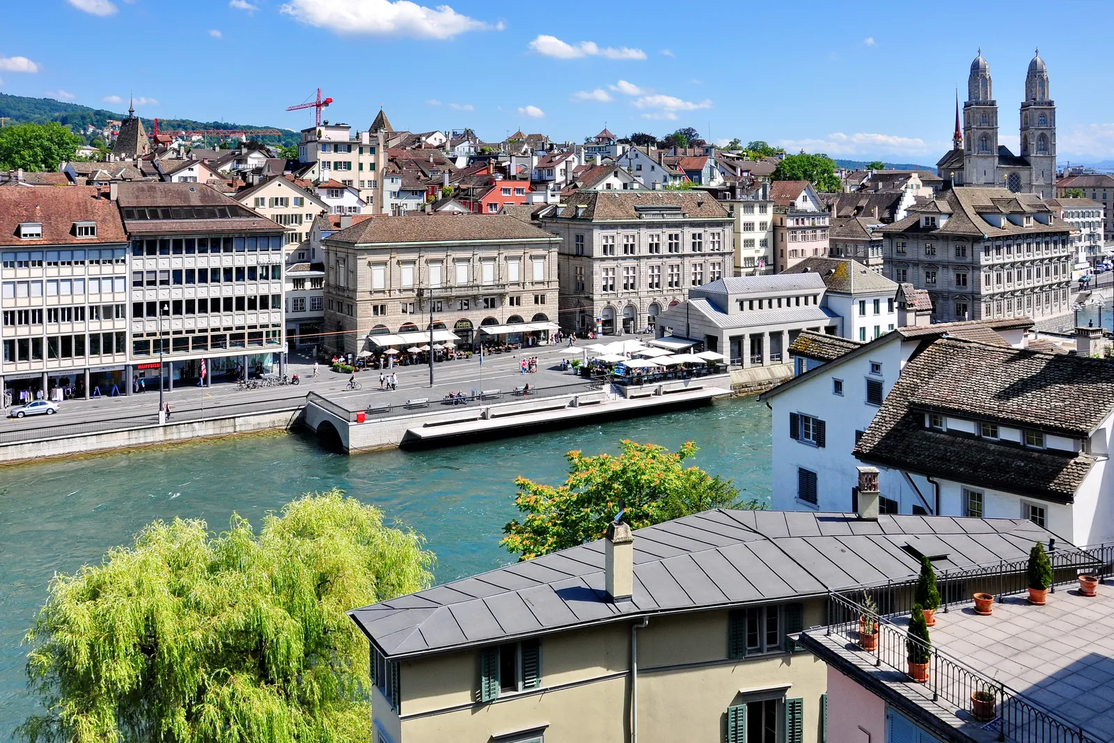 The view from the Lindenhof terrace in Zurich over the Limmat to the right-bank old town, with the Rathaus on the quay, tightly packed roofs behind it and the Grossmünster's twin towers on the skyline