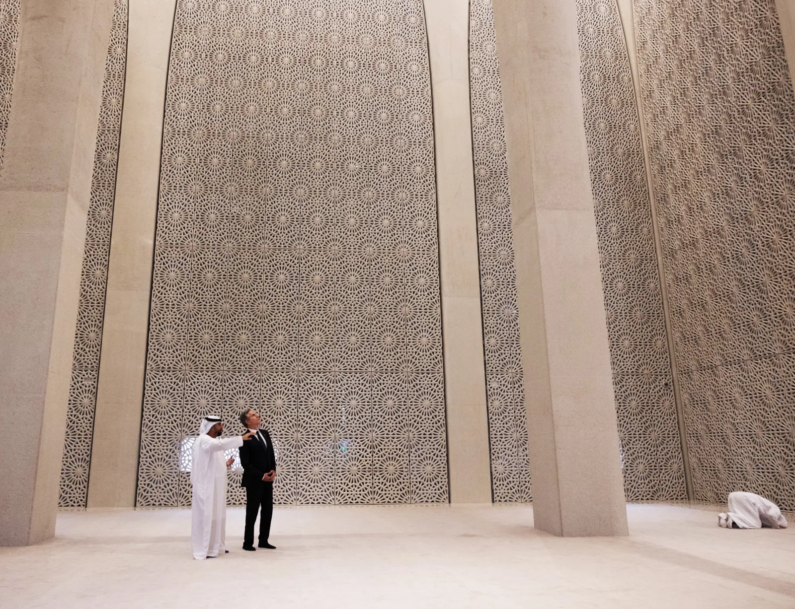 The interior of the Imam Al-Tayeb Mosque at the Abrahamic Family House, a tall pale room whose walls are formed of vertical screens cut in repeating circular patterns