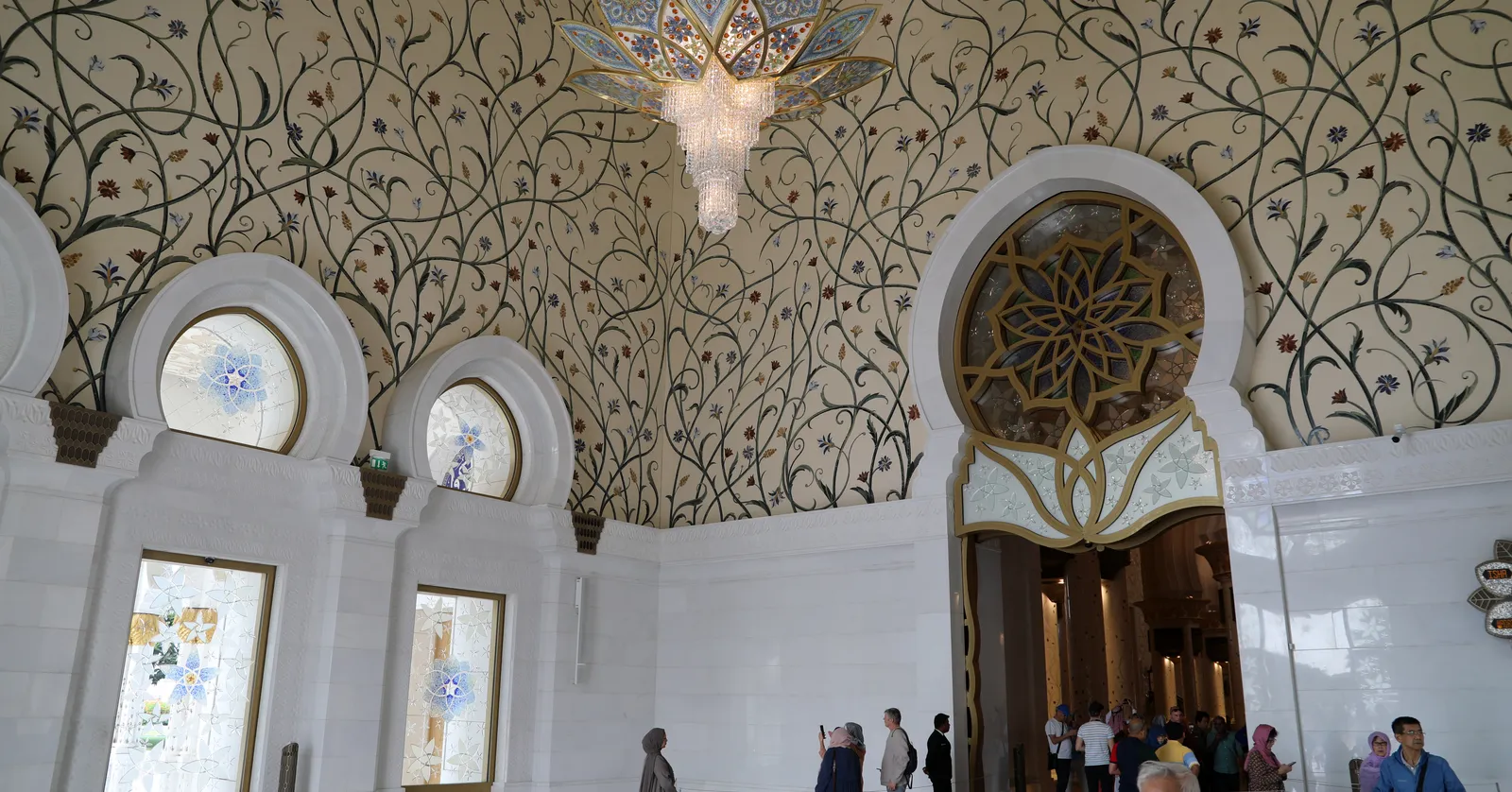 The southern atrium of Sheikh Zayed Grand Mosque, its vault covered in gold vine and flower inlay, with a flower-shaped crystal chandelier hanging above an ornate gilded doorway
