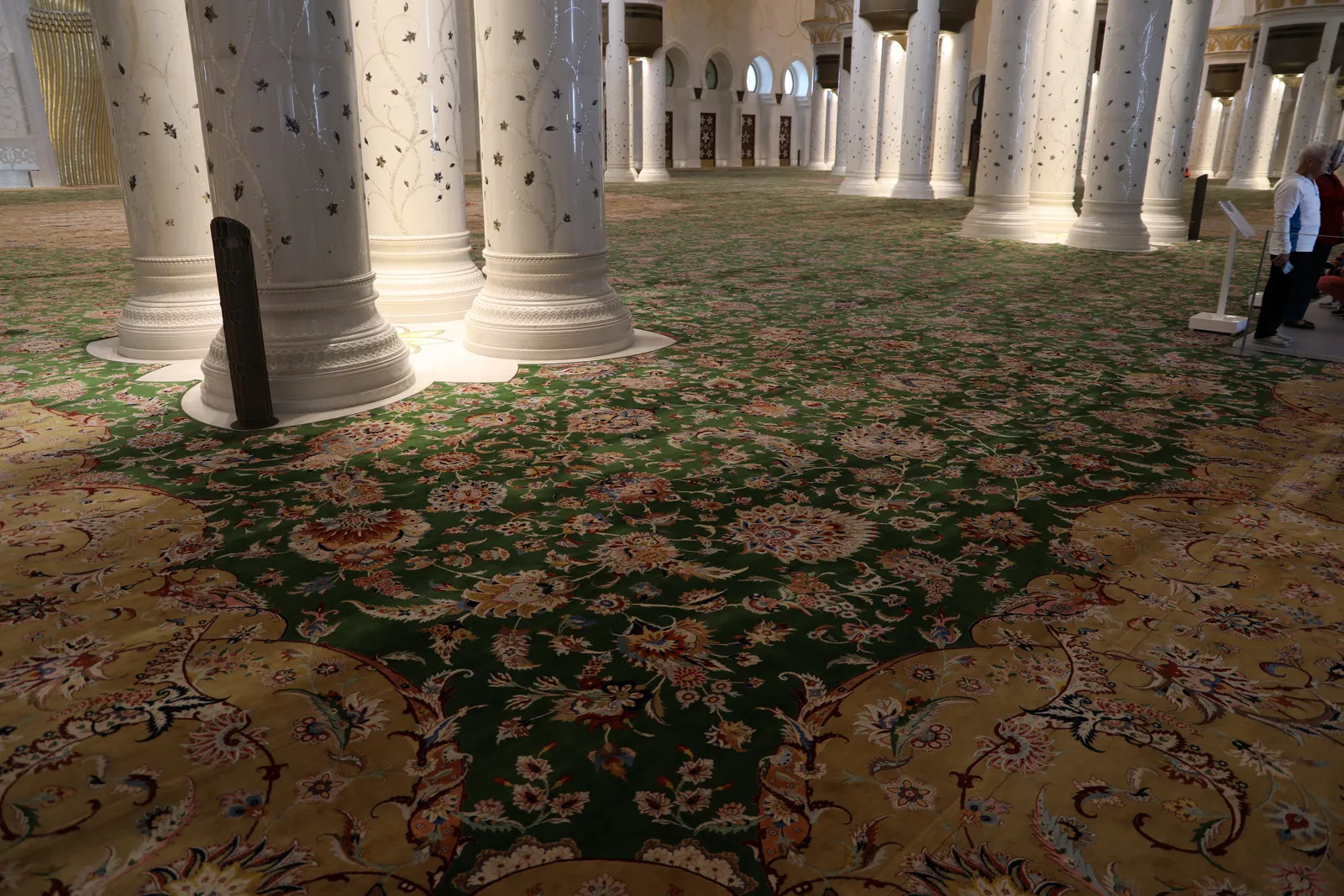 The green and gold floral carpet of the main prayer hall at Sheikh Zayed Grand Mosque running away between rows of inlaid marble columns