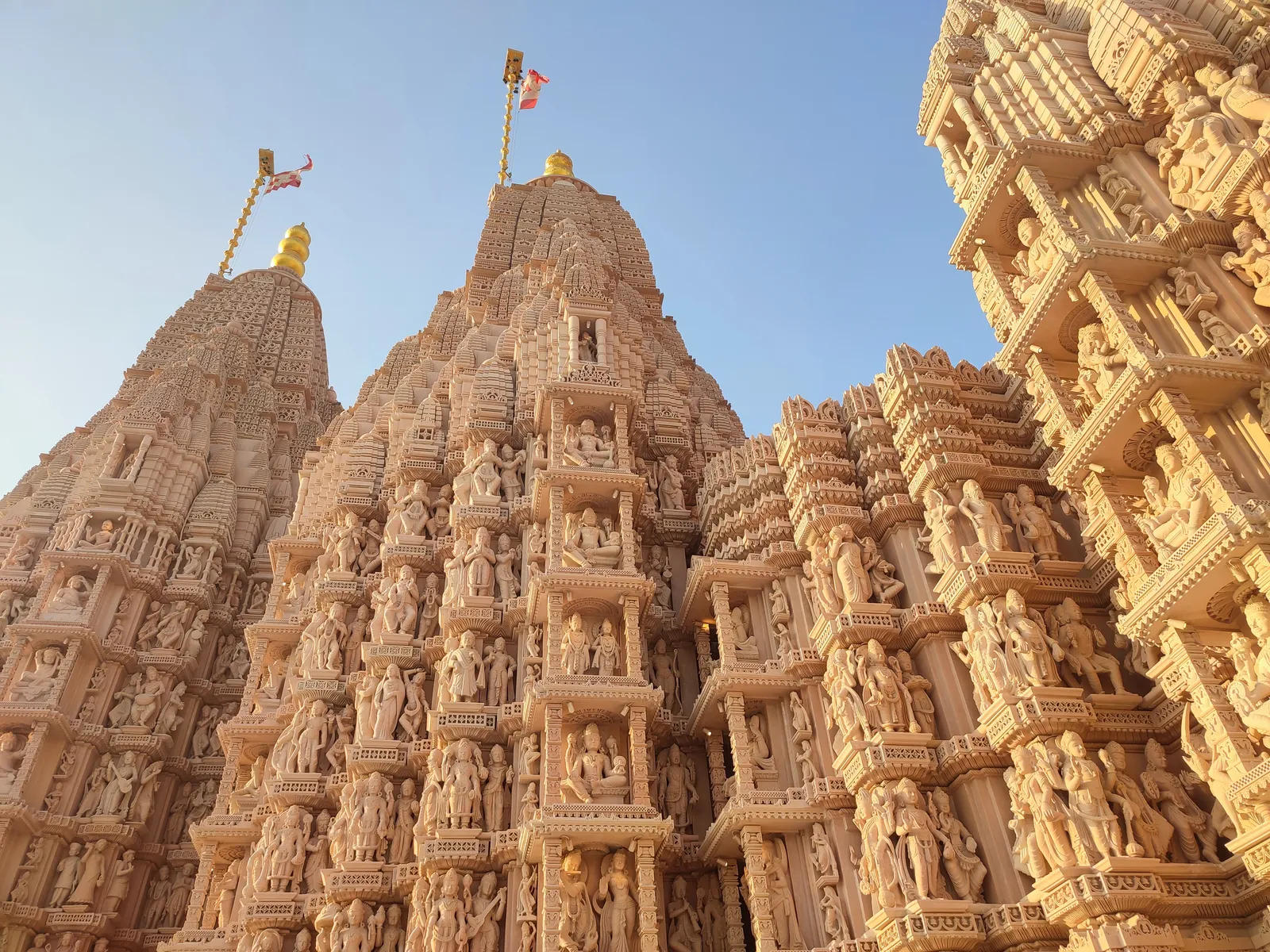Carved sandstone spires of the BAPS Hindu Mandir near Abu Dhabi, covered from base to tip in rows of small figures, with gold finials and flags against a clear sky