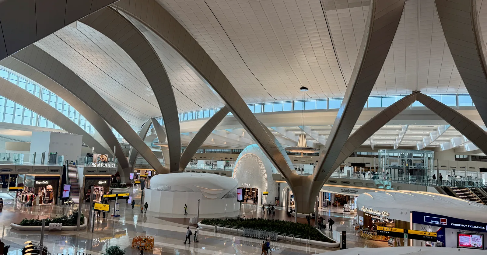 The departure hall of Terminal A at Zayed International Airport in Abu Dhabi, with white concrete arches branching overhead like palm fronds above the shopping level