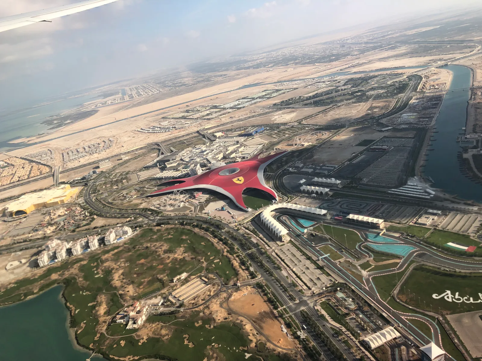 Yas Island seen from the air on the approach to Abu Dhabi, with the red star-shaped roof of Ferrari World in the middle, the marina circuit beside it and desert running to the horizon