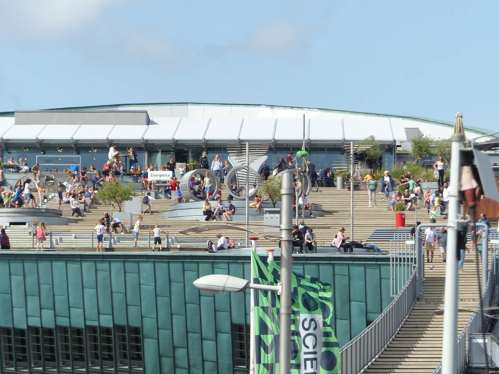 The wide stepped public rooftop of the NEMO Science Museum in Amsterdam, busy with people sitting on its terraced steps above the building's green copper flank
