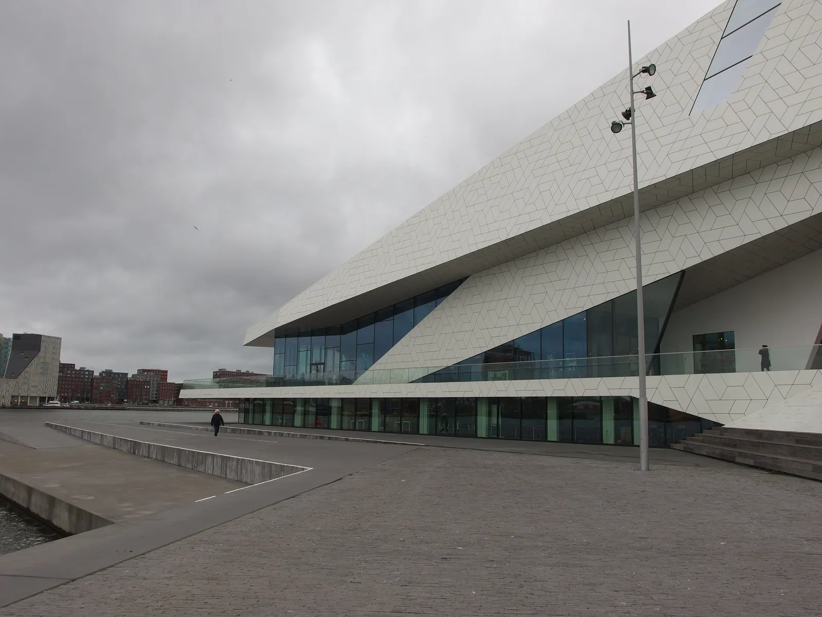 The Eye Filmmuseum on the north bank of the IJ in Amsterdam, a sharply angular white building with faceted panels and sloping glass walls, seen from the empty waterfront square in front of it