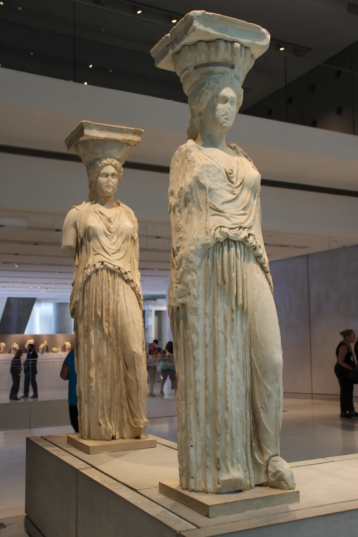 Two of the original Erechtheion Caryatids standing on plinths in the Acropolis Museum in Athens, draped figures carrying capitals on their heads