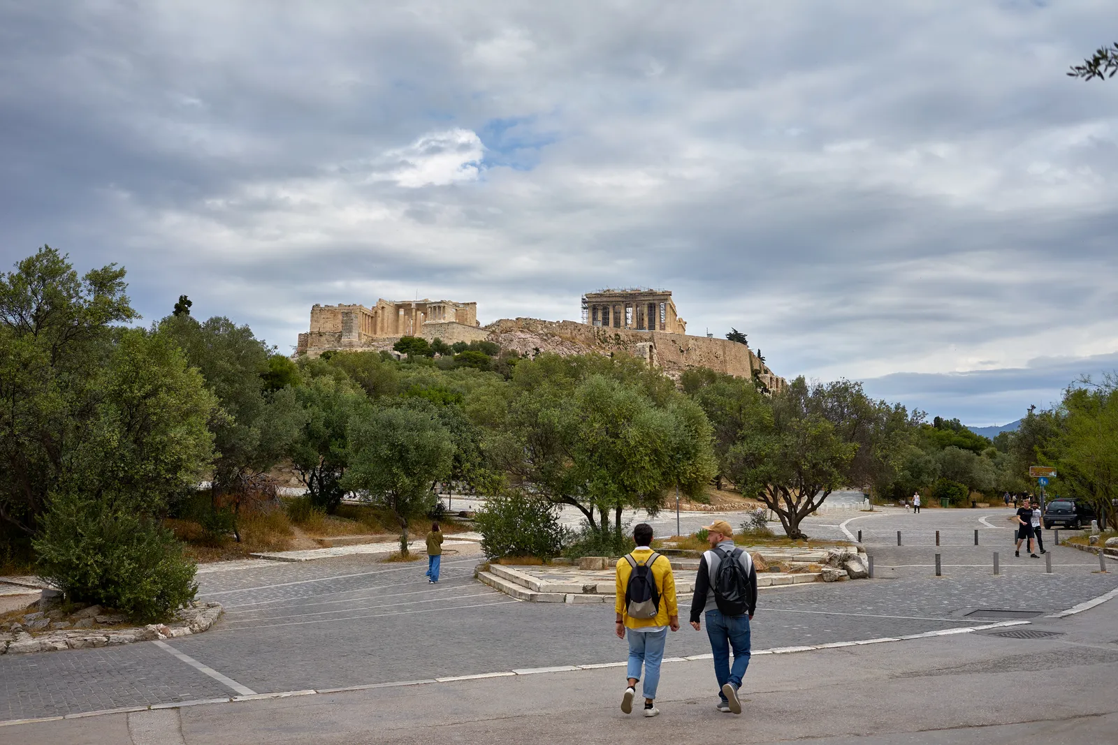 Two people walking up the empty pedestrian street of Dionysiou Areopagitou in Athens with the Acropolis rock and the Parthenon on the ridge above