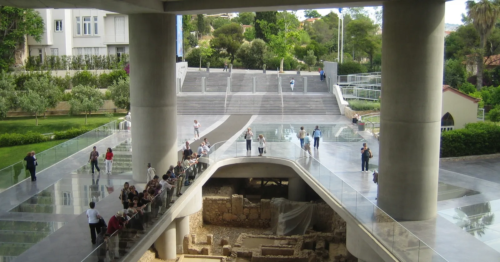 The forecourt of the Acropolis Museum in Athens, where visitors walk on a glass floor set over the excavated ruins beneath the building