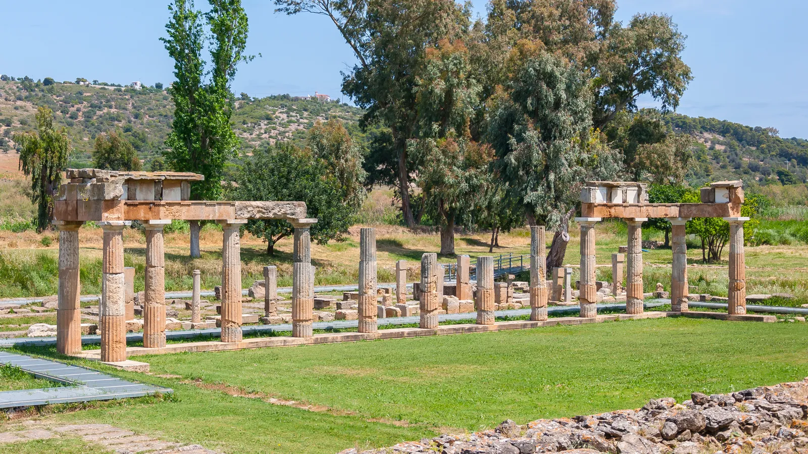 The restored colonnade of the Sanctuary of Artemis at Brauron standing in a green meadow with wooded hills behind
