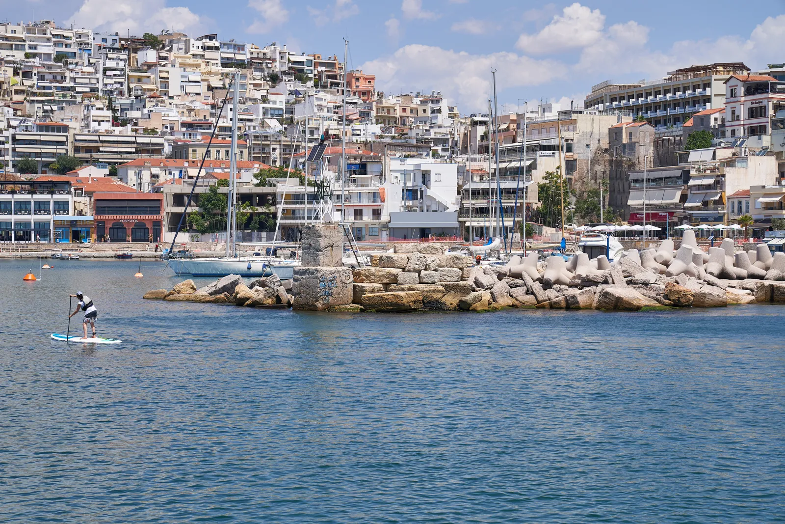 Weathered stone remains of the ancient harbour wall standing in the water at the entrance to Mikrolimano in Piraeus