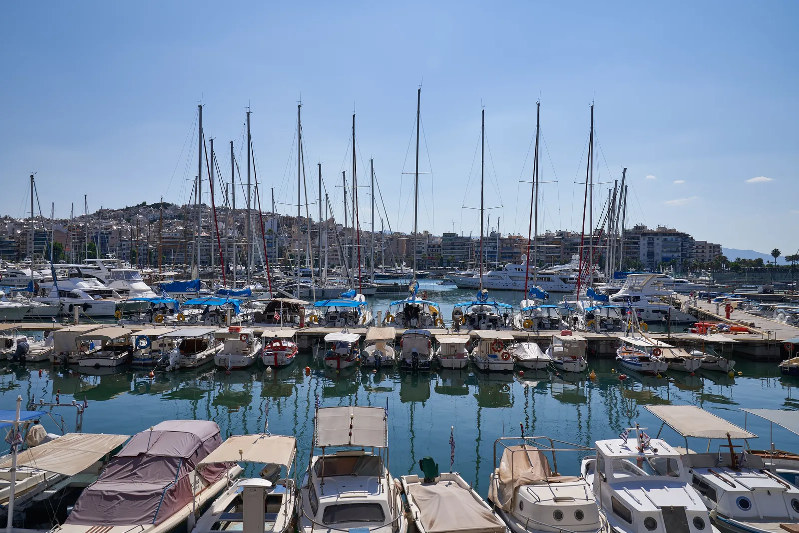 Rows of yachts and small boats moored in Zea Marina in Piraeus under a clear sky, with apartment blocks along the far shore