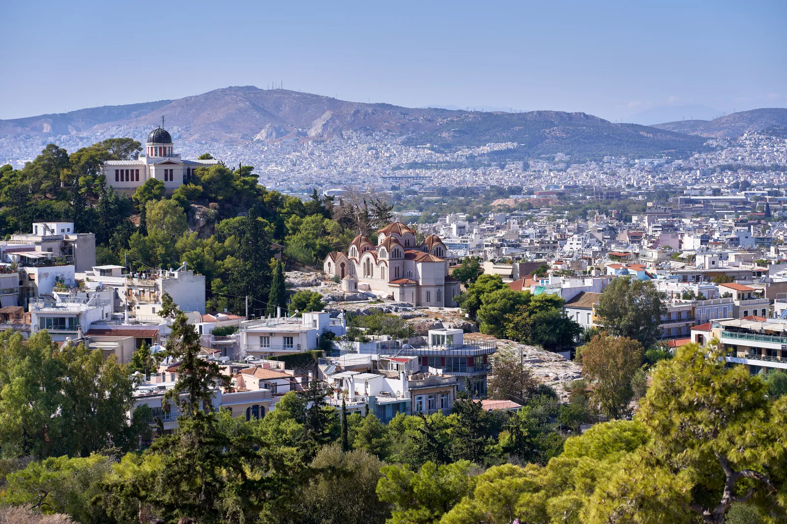 The white domed building of the National Observatory of Athens on the wooded Hill of the Nymphs, with the church of Agia Marina below it and the city spreading out behind