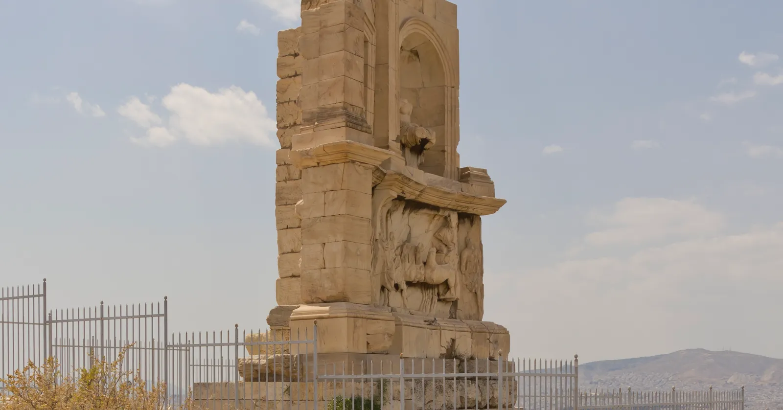 The Roman funerary monument to Philopappos standing on the bare summit of Filopappou hill in Athens behind an iron railing