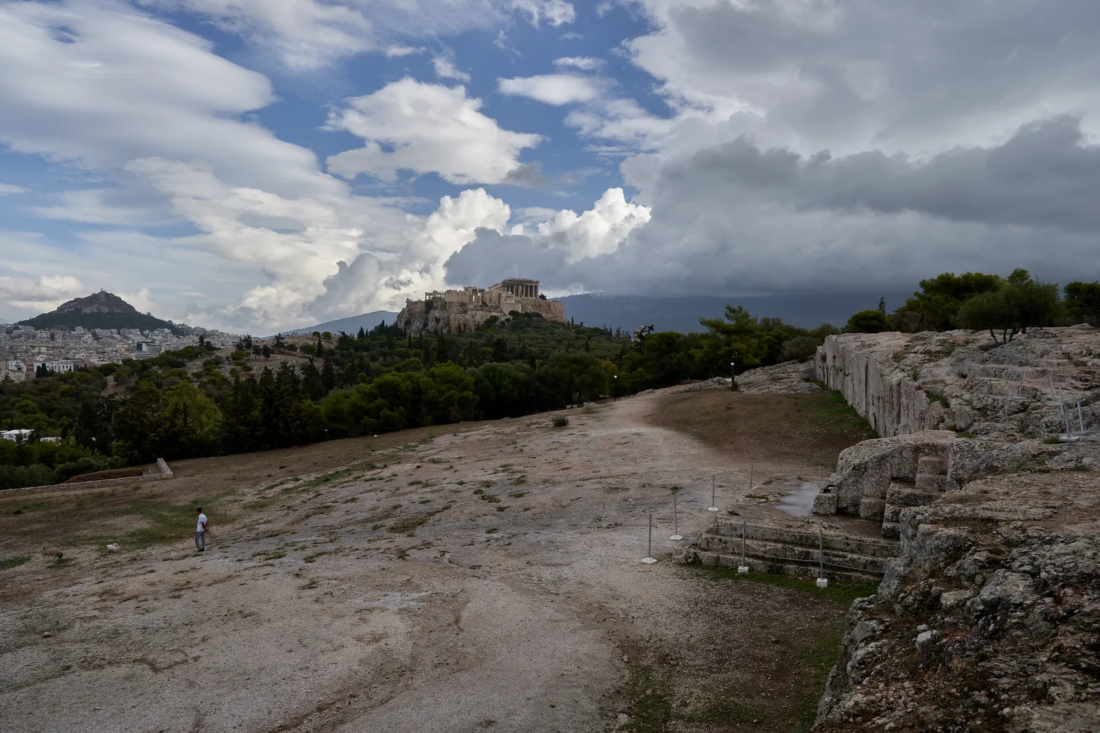 The bare rock plateau of the Pnyx in Athens with the cut retaining wall to the right and the Acropolis and Lycabettus hill in the distance