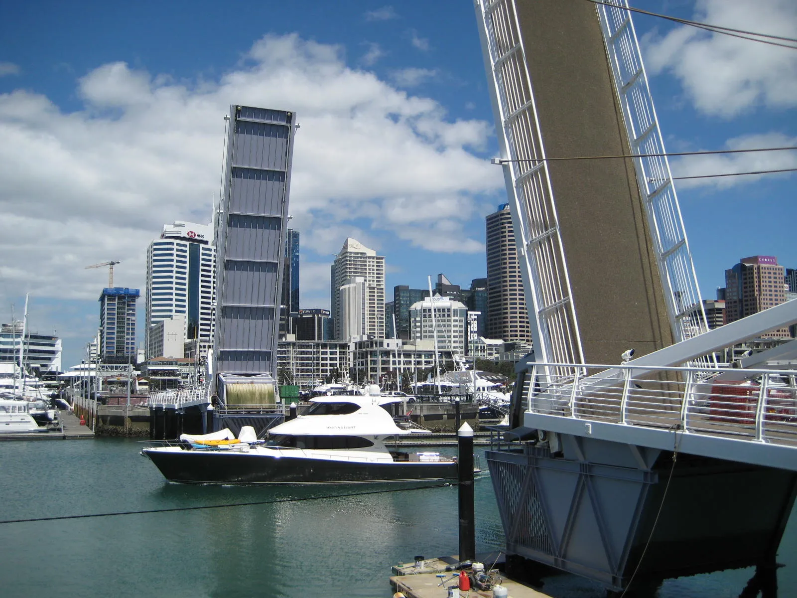 One span of the Wynyard Crossing footbridge in Auckland raised upright to let a motor launch pass through, with the city center's towers behind