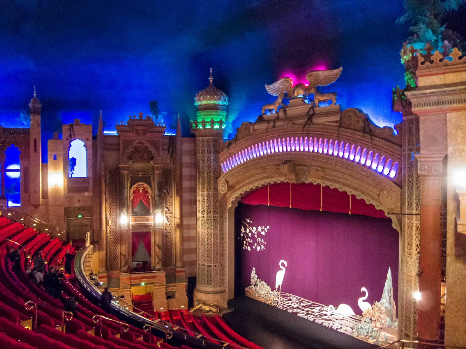 The auditorium of the Civic Theatre in Auckland, a Moorish proscenium with a green domed minaret and gilded winged panthers under a deep blue ceiling lit to look like a night sky, red seats curving below