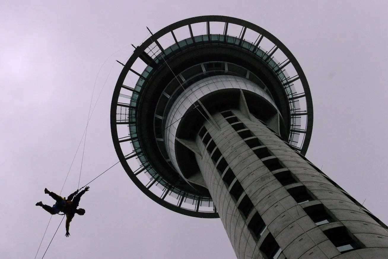 Looking straight up the shaft of Auckland's Sky Tower to its circular observation pod, with a harnessed person descending on a wire away from the side of it