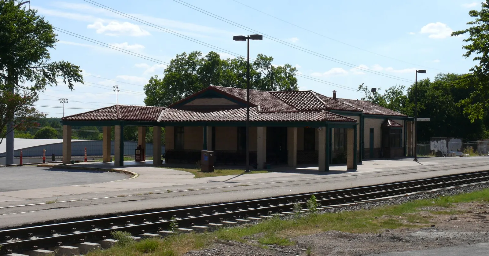 The Austin Amtrak depot, a long low brick building with a red tile roof and an open platform canopy on square columns, standing beside the running rails with trees behind it