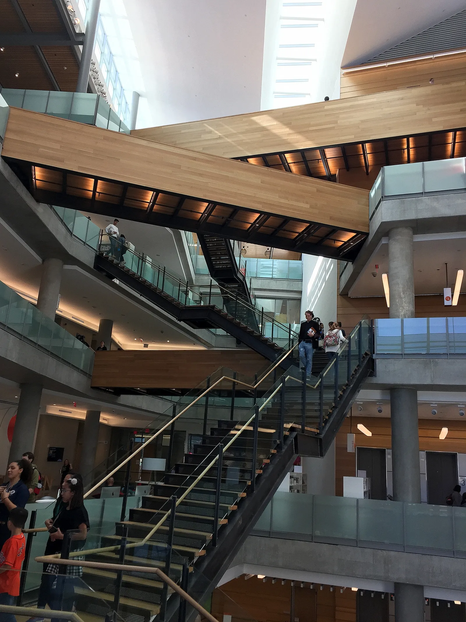 The atrium inside Austin Central Library, open stairs crossing back and forth between six floors under timber-lined soffits and a high white ceiling, with people on the landings