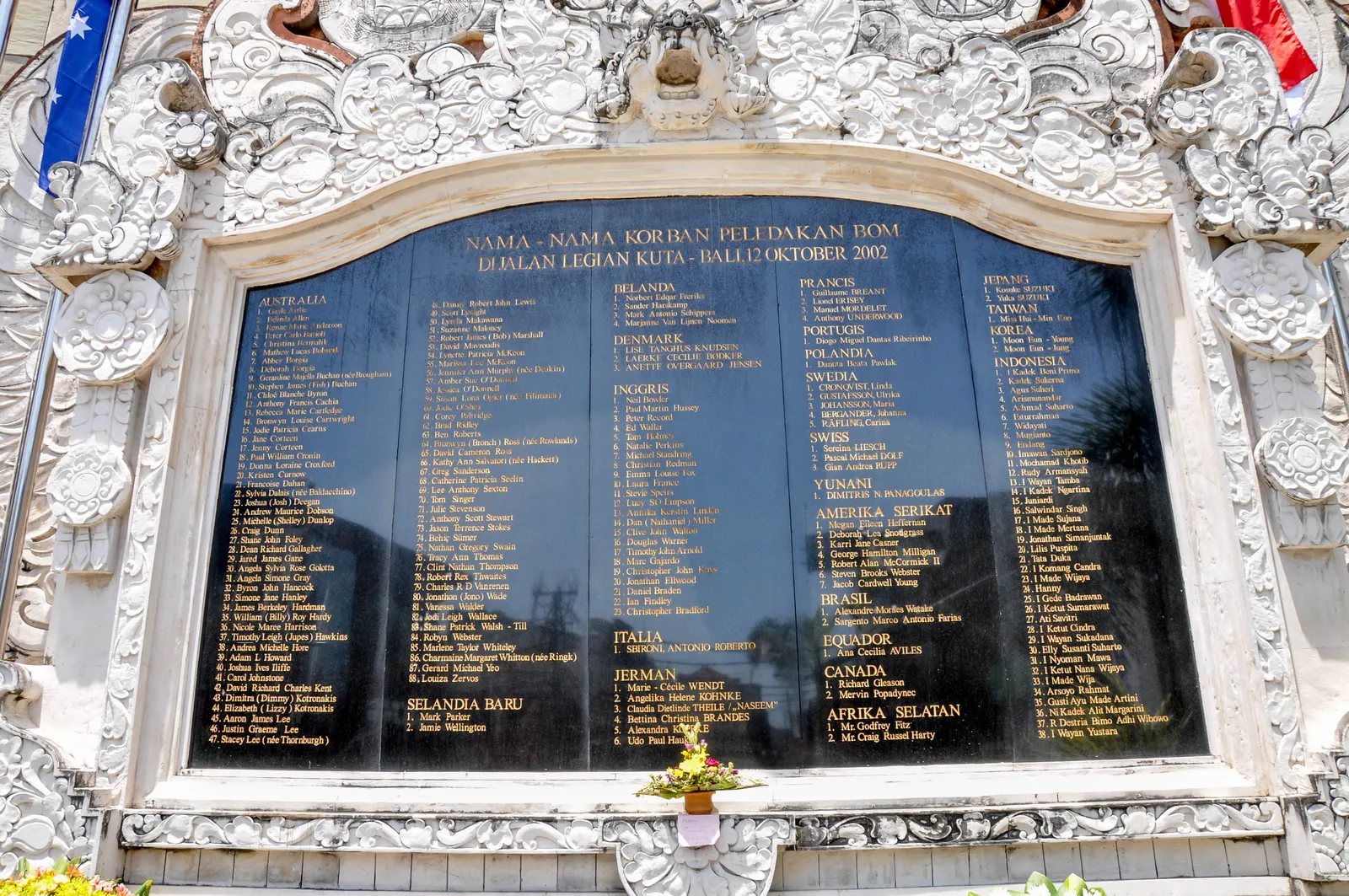 The black marble plaque on the Bali bombing memorial on Jalan Legian, listing victims' names grouped under their countries inside a carved white stone frame