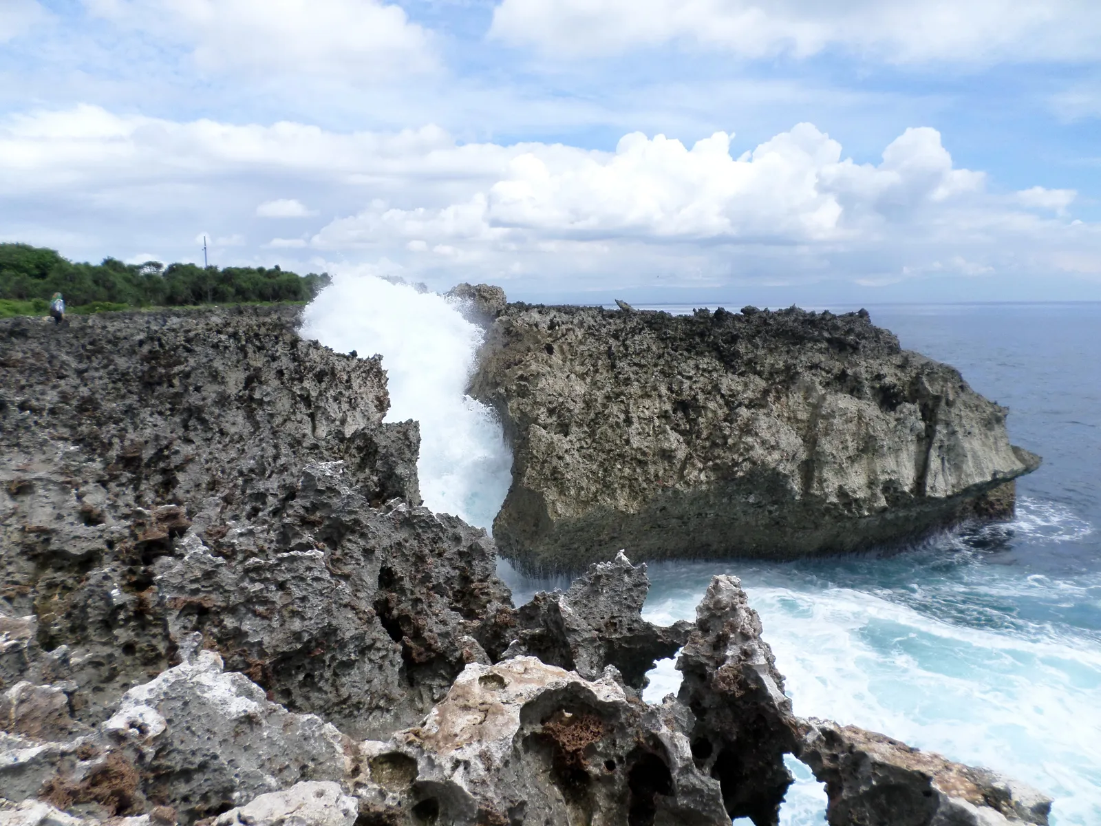 White spray bursting upward out of a narrow gap in the eroded limestone headland at Water Blow in Nusa Dua, Bali, with open sea to the right