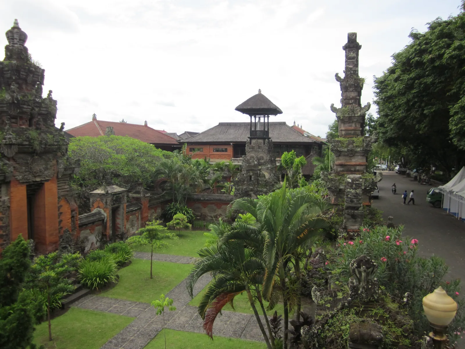 A planted courtyard inside the Bali Museum in Denpasar, with brick and stone gateways, a tiered pavilion and carved shrines between palms and lawns