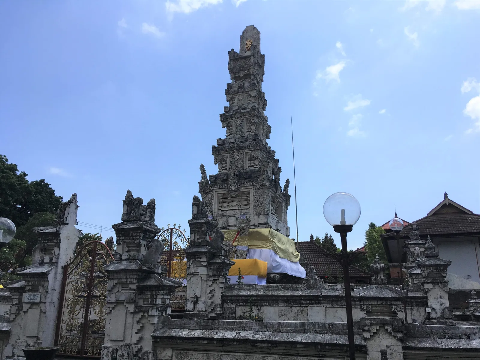 The tall white coral padmasana shrine of Pura Jagatnatha in Denpasar rising above the temple's carved walls, draped in yellow and white cloth