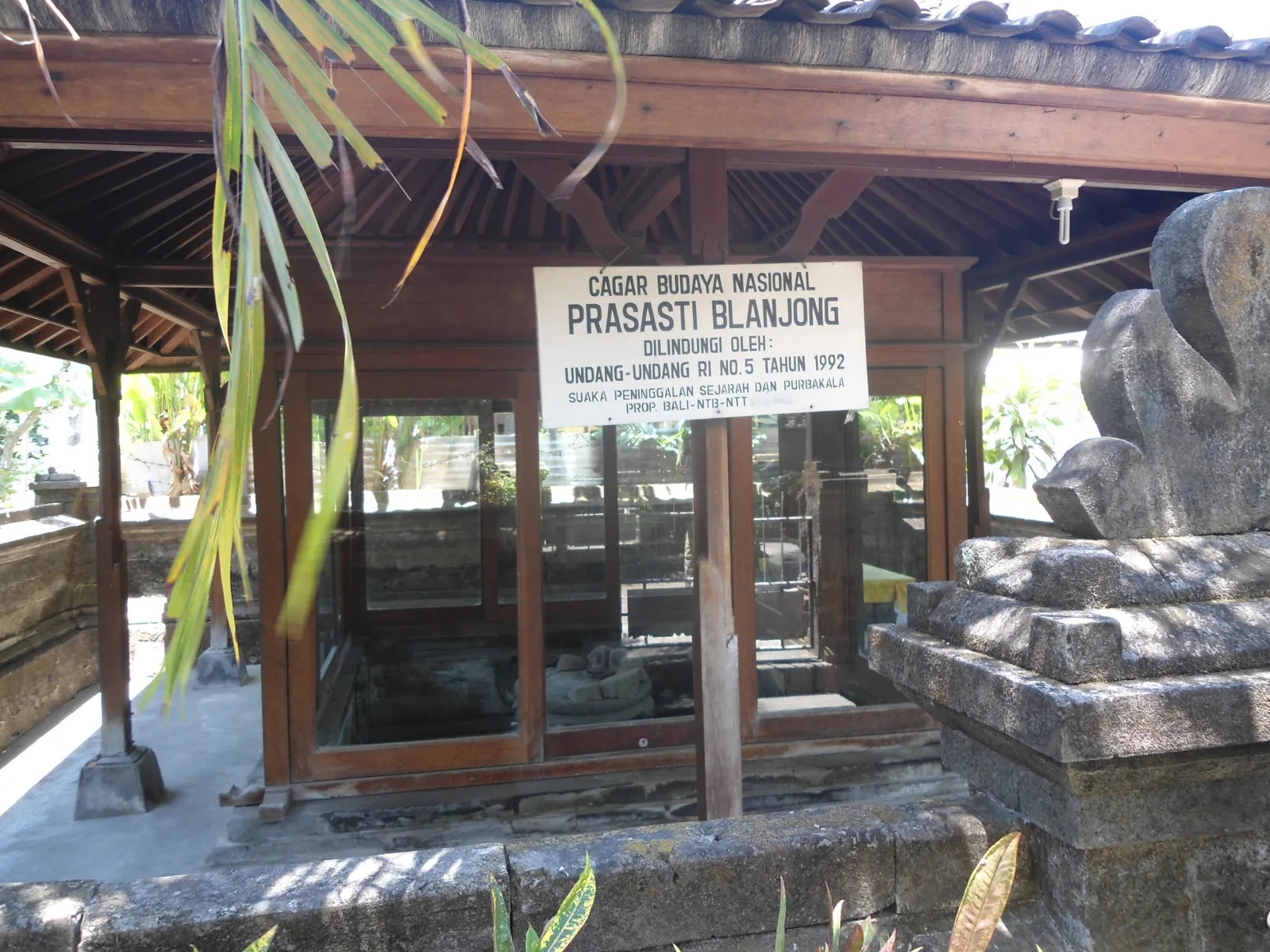 The open timber pavilion over the Blanjong pillar in Sanur, its national heritage sign reading Prasasti Blanjong above the glassed pit the stone stands in