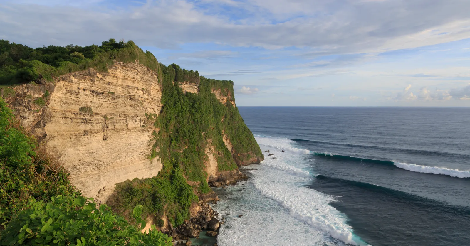 The green-topped limestone cliffs of the Bukit peninsula at Uluwatu in Bali, dropping into lines of white surf rolling in from the Indian Ocean