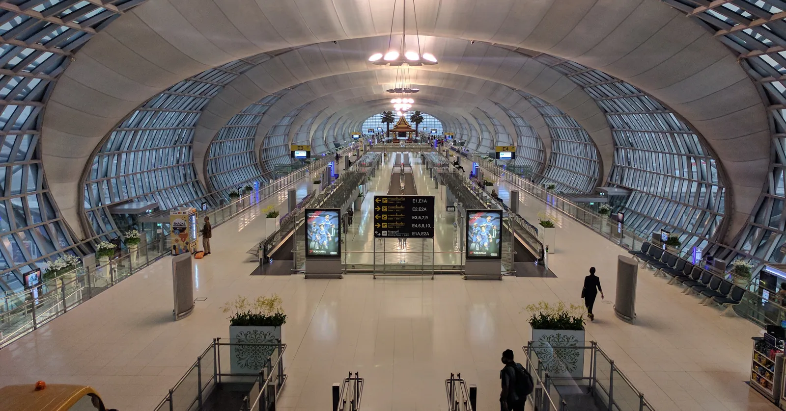 The vaulted concourse at Suvarnabhumi Airport in Bangkok, a symmetrical barrel of glass and white steel ribs running away over a polished floor with a departure board in the middle distance