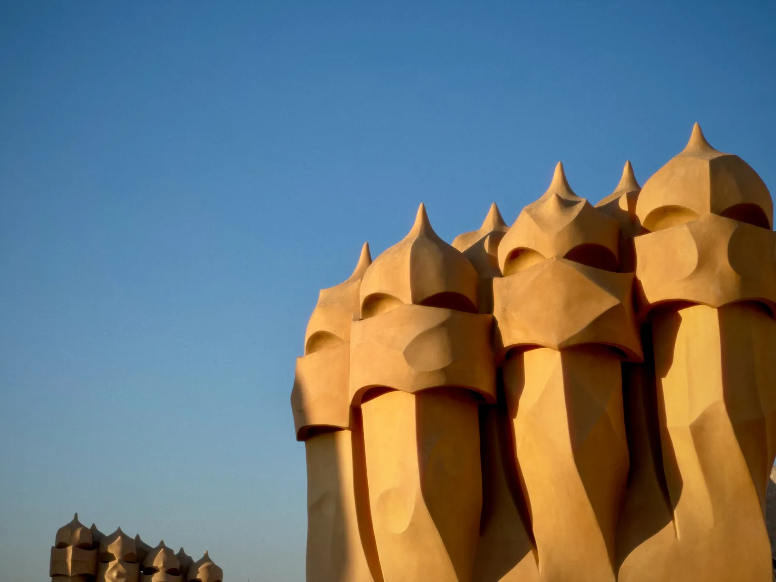 Helmet-shaped chimneys on the rooftop terrace of La Pedrera in Barcelona, glowing ochre against a clear blue sky