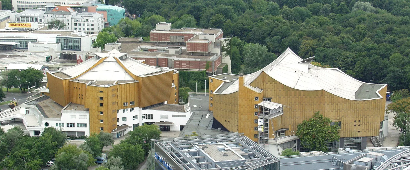 The Berlin Philharmonie and the smaller Chamber Music Hall seen from above, two gold-clad buildings with irregular tent-shaped roofs surrounded by trees