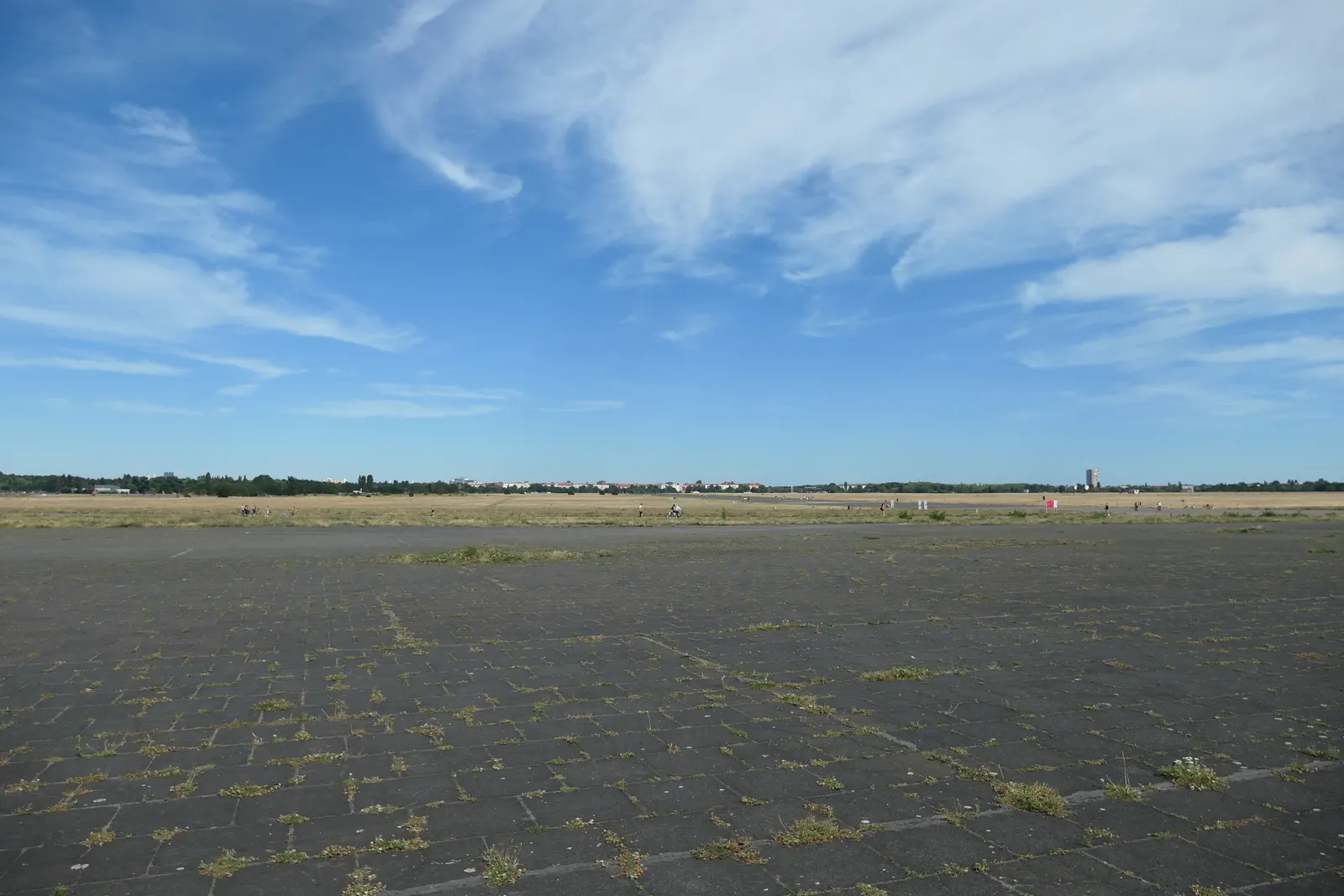 The open expanse of Tempelhofer Feld in Berlin, a weathered concrete airfield apron running flat to a distant treeline under a wide sky with streaked cloud