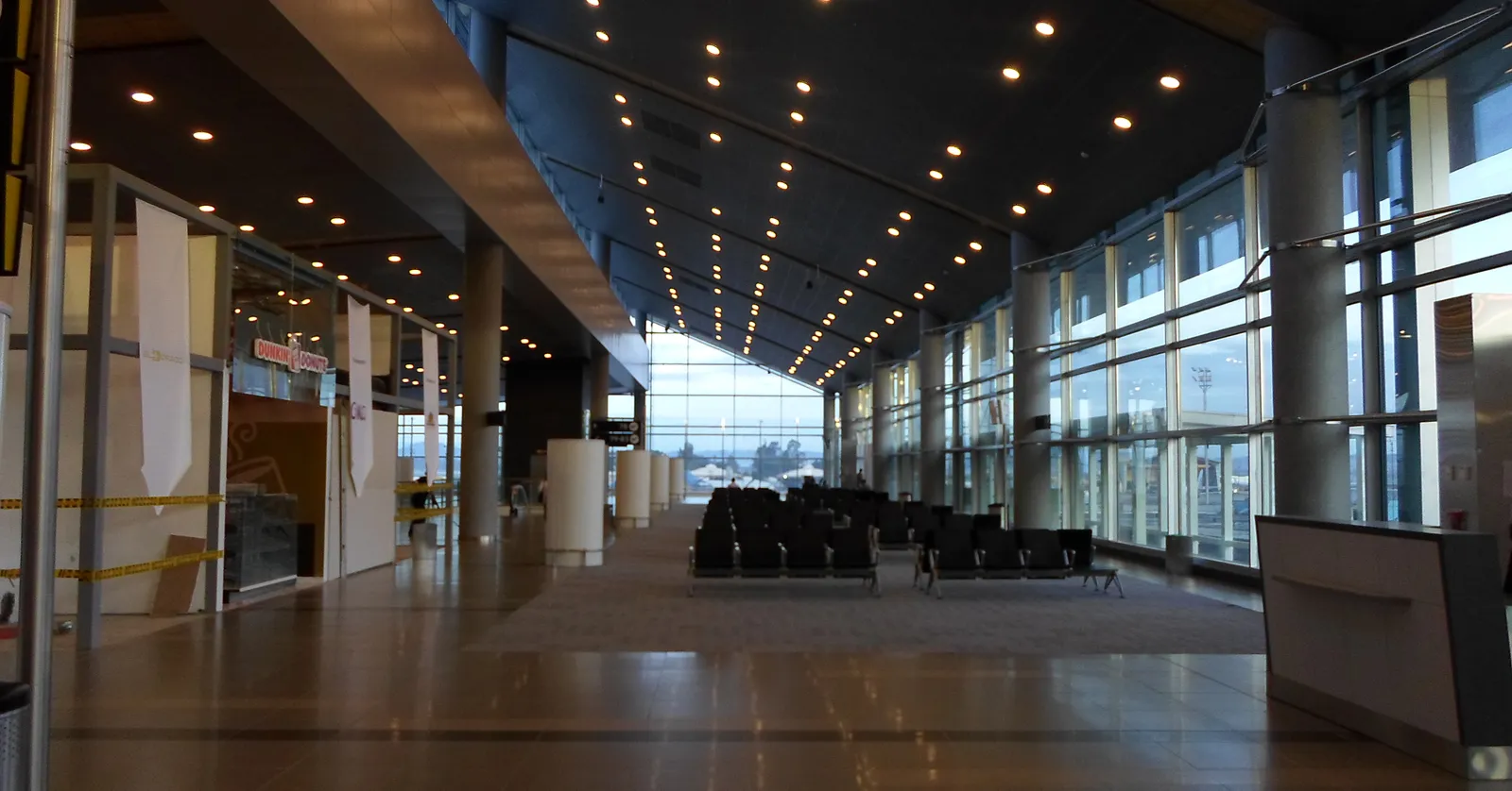 The domestic concourse at Bogotá's El Dorado airport, a long hall with a curved glass wall down one side, rows of black seating and aircraft visible on the apron outside