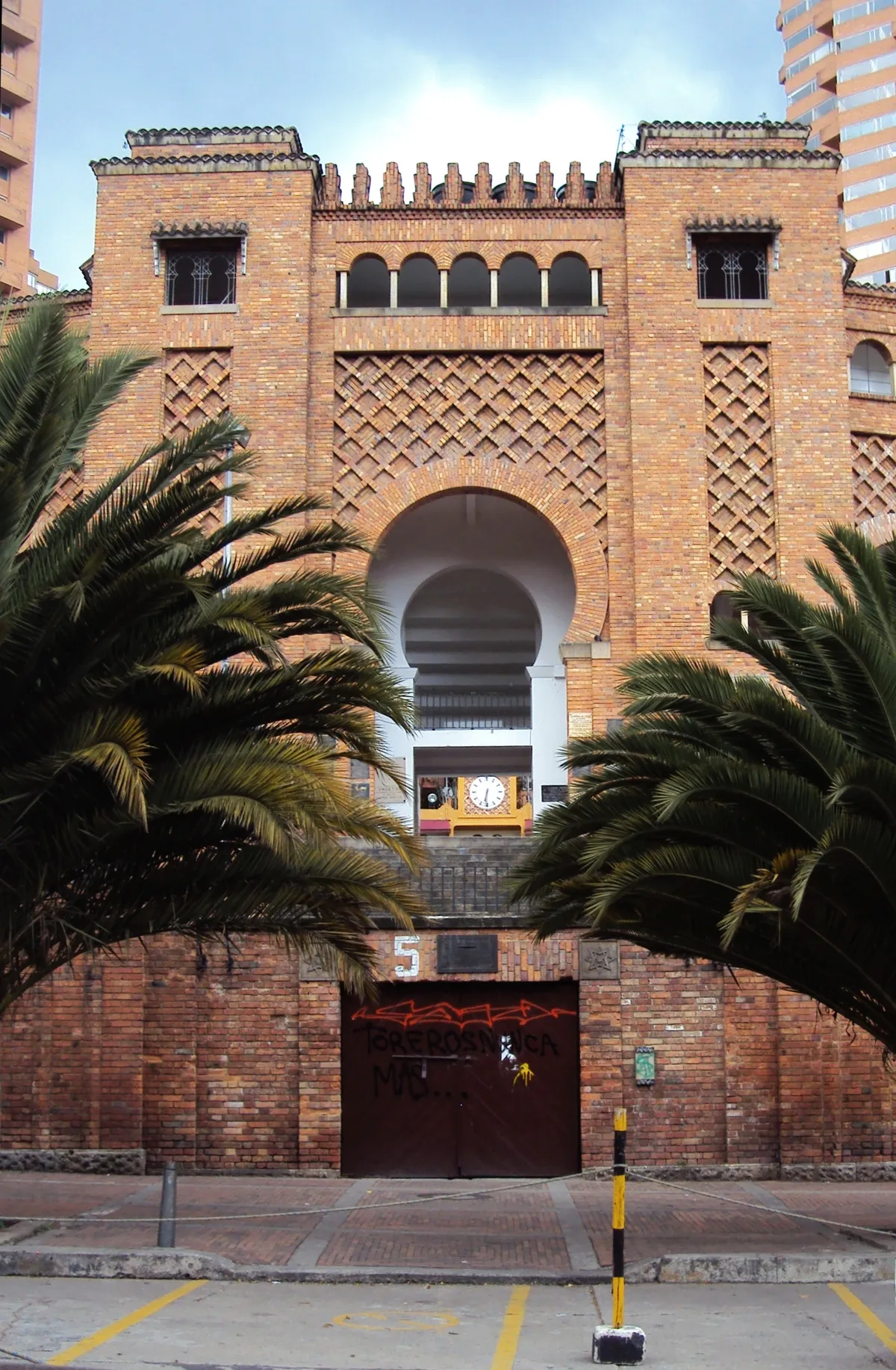 The main entrance of the Santamaría bullring in Bogotá, a tall brick front with a horseshoe arch, latticed brickwork panels and crenellations along the top, framed by two palms